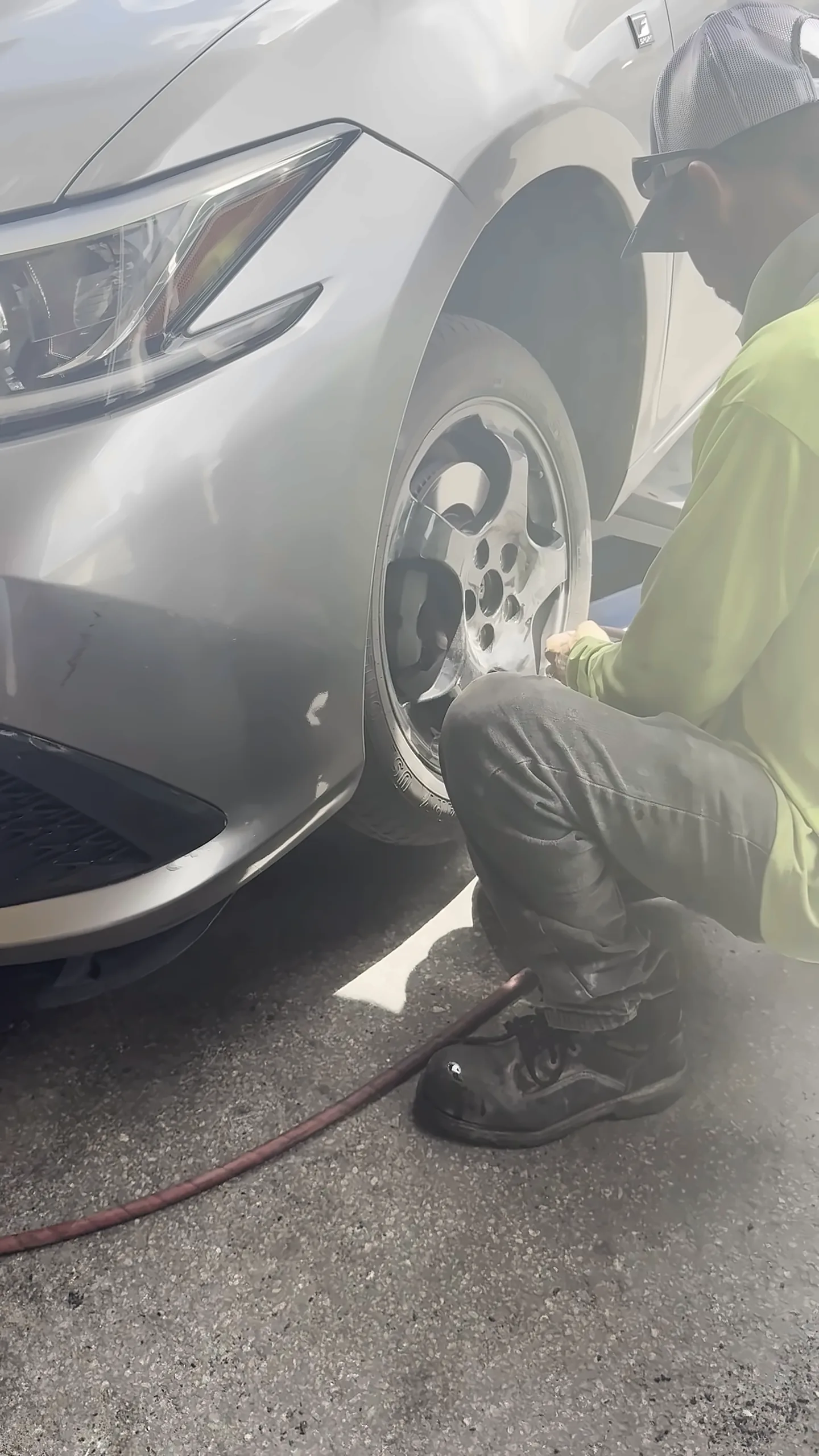 Técnico agachado junto a la rueda delantera de un carro plateado con una manguera de aire